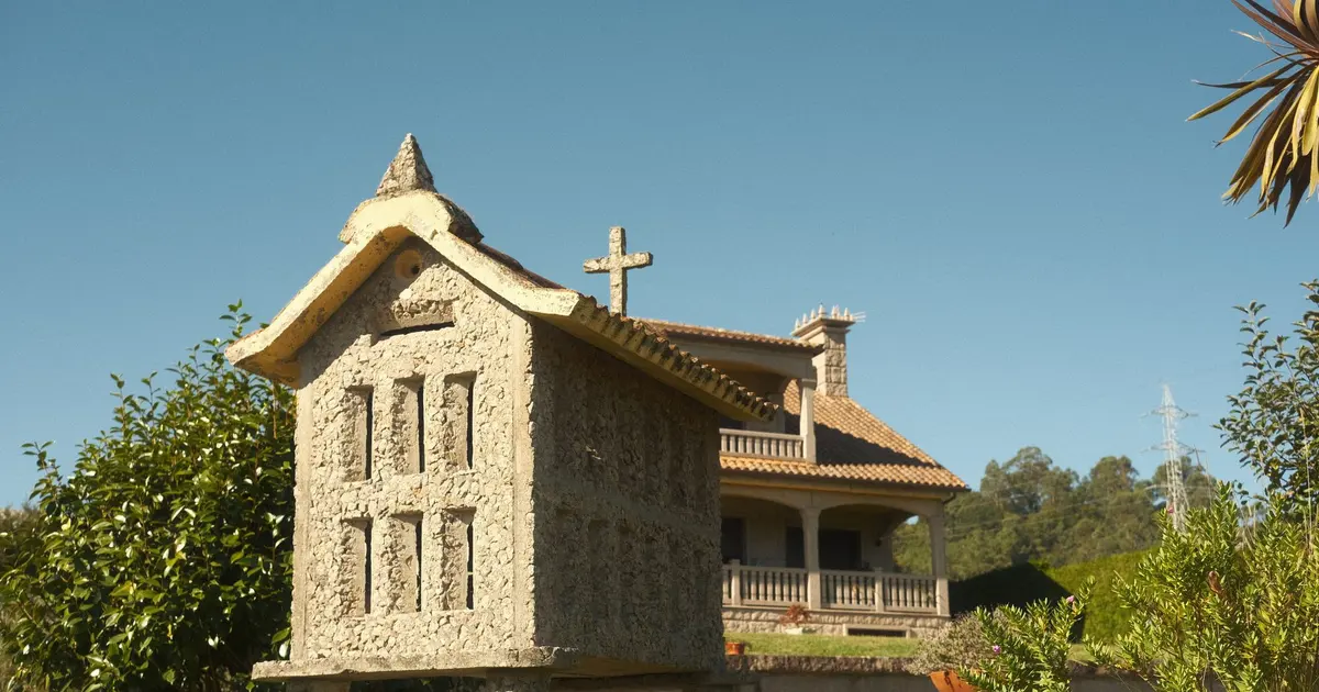 Hórreo tradicional gallego junto a una casa de campo con prado